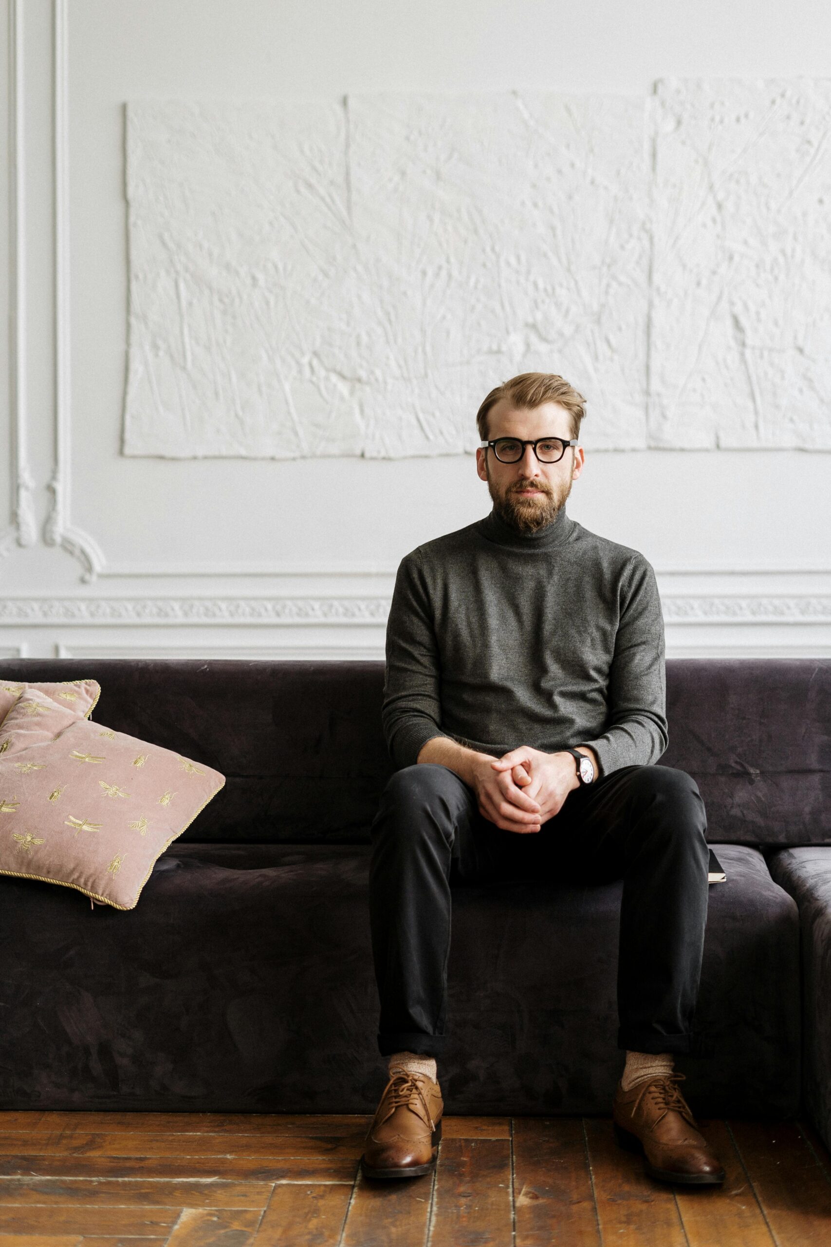 Man sitting on a couch in a minimalist room, reflecting a calm and professional demeanor.